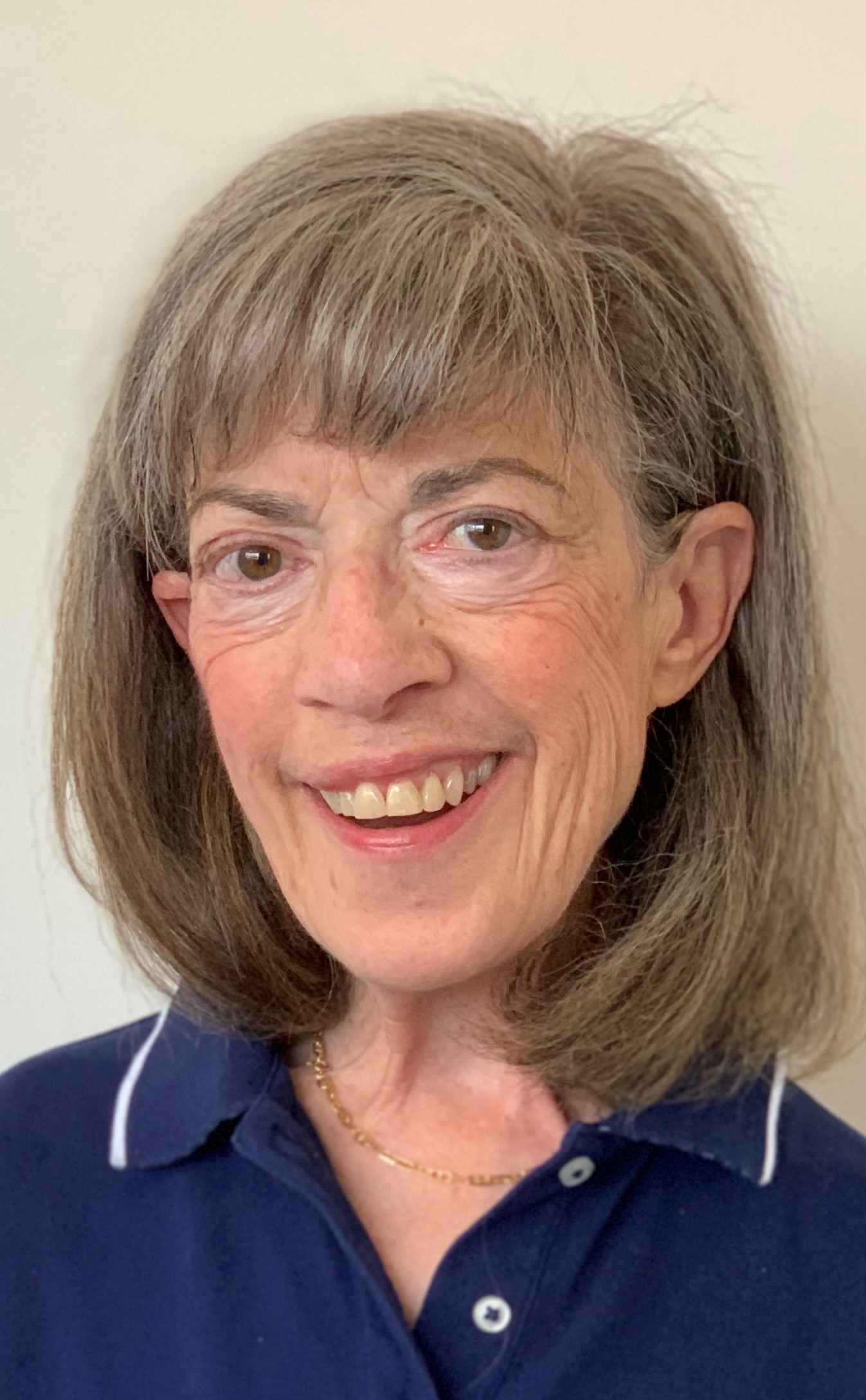 June Kailes (she, her)  smiling, wearing a red jacket, graying hair